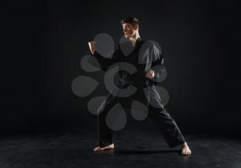 Male karate fighter in black kimono, combat stance, dark background. Man on workout, martial arts