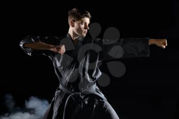 Male karate fighter in black kimono, combat stance, dark background. Man on workout, martial arts, fighting competition