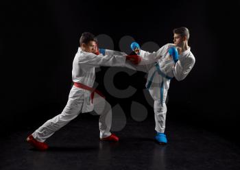 Two male karatekas in white kimono and gloves, strike in action, dark background. Fighters on workout, martial arts, fighting competition