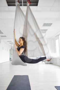Aerial yoga, slim woman poses on hammock. Fitness, pilates and dance exercises mix. Female person on yogi workout in sports studio