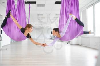 Aerial or fly yoga studio, female group training, hanging on hammocks. Fitness, pilates and dance exercises mix. Women on yogi workout in gym