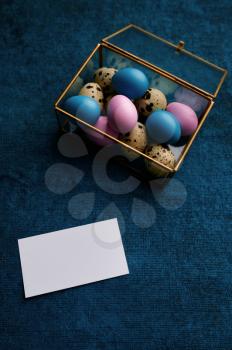 Easter eggs in decorative gift box and greeting card on blue cloth background. Paschal food, event decoration, spring holiday celebration symbol