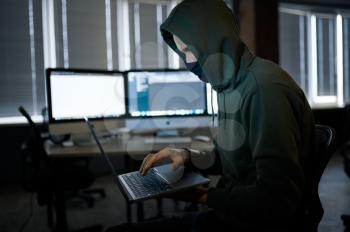 Male internet hacker in hood holds laptop, front view. Illegal web programmer at workplace, criminal occupation. Data hacking, cyber safety