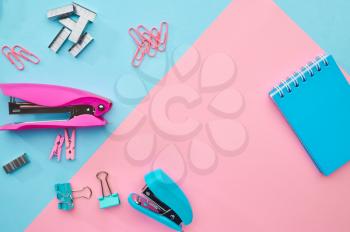 Stapler and paper clips closeup, blue and pink background. Office stationery supplies, school accessories