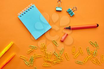 Paper clips, notepad and marker closeup on orange background. Office stationery supplies, school or education accessories, writing and drawing tools