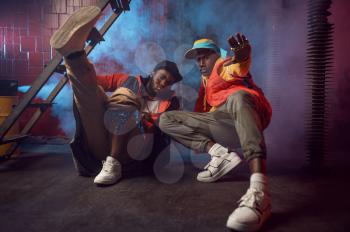 Two serious rappers with gold jewelry poses in cool studio, underground decoration. Hip-hop performers, trendy rap singers, break-dancers