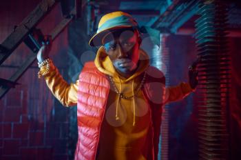Stylish rapper in yellow hoodie posing in grunge studio with cool underground decoration. Hip-hop performer, rap singer, break-dance performance