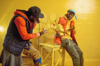 Two stylish rappers poses in cool studio, yellow background. Hip-hop performers, trendy rap singers, break-dancers