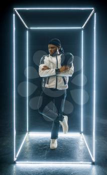 Rapper posing in illuminated cube, dark background. Hip-hop performer, rap singer, break-dance performing, entertainment lifestyle, breakdancer