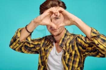 Young man shows heart sign, blue background, emotion. Face expression, male person looking on camera in studio, emotional concept, feelings