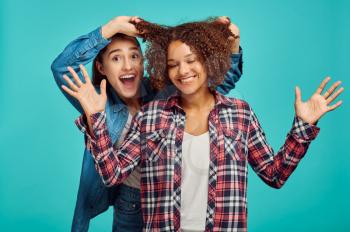 Two young cheerful women, blue background, positive emotion. Face expression, female person looking on camera in studio, emotional concept, feelings