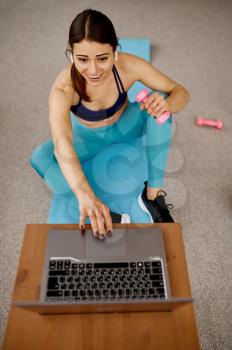 Girl sitting at the laptop, online fit training. Female person in sportswear, internet sport workout, room interior on background
