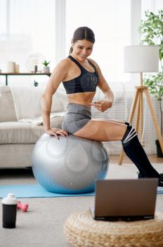 Woman doing exercise with ball, online pilates training at the laptop. Female person in sportswear, internet sport workout, room interior on background