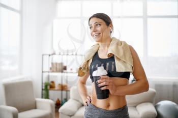 Woman holds water bottle after training. Female person in sportswear, internet sport workout, room interior on background