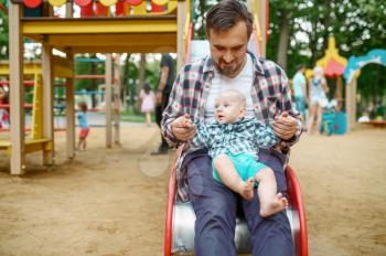 Happy parents play with little baby on playground in summer park. Mom and dad leisures with male kid, picnic with child in the forest