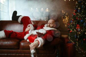 Bad drunk Santa claus lying on sofa, hangover after nasty party, humor. Unhealthy lifestyle, bearded man in holiday costume, new year and alcoholism