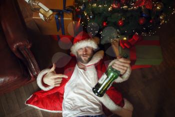 Bad drunk Santa claus in underpants lying under christmas tree, nasty party, humor. Unhealthy lifestyle, bearded man in holiday costume, new year and alcoholism
