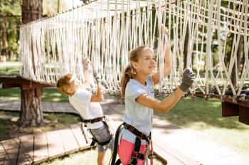 Little brave kids climbs on net in rope park, playground. Children climbing on suspension bridge, extreme sport adventure on vacations, danger entertainment outdoors