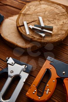 Stapler and staples on stump, closeup, wooden background, nobody. Professional instrument, carpenter equipment, woodworker tools
