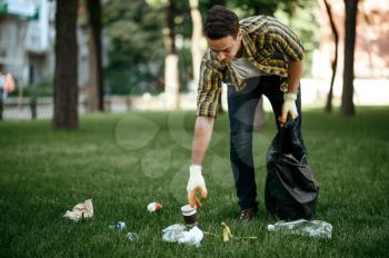 Young man collects garbage in a bag in park, volunteering. Male person cleans forest, ecological restoration, eco lifestyle, trash collection and recycling, ecology care, cleaning