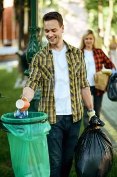 Young man puts garbage in plastic bag in park, volunteering. Male person cleans forest, ecological restoration, eco lifestyle, trash collection and recycling, ecology care, environment cleaning