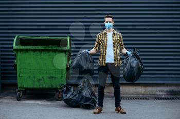 Volunteer in mask holds plastic trash bags outdoors, volunteering. People cleans city streets, ecological restoration, garbage collection and recycling, ecology care, environment cleaning