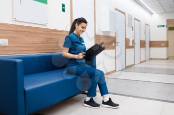 Female surgeon with notebook sitting on sofa in clinic hall, surgery. Doctor in uniform, medical worker, medicine and health, professional healthcare in hospital