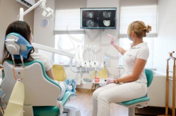 Female dentist shows to patient x-ray of teeth, stomatology clinic. Doctor in uniform, medical worker, stomatologist, medicine and health, professional dental mouth care and hygiene, dentistry