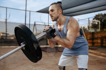 Muscular man prepares barbell weights for exercise, street workout. Fitness training on sports ground outdoor, male person pumps muscles