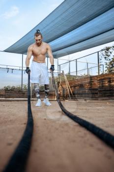Muscular man doing exercise with ropes, street workout, crossfit. Fitness training on sports ground outdoor, male person pumps muscles, active urban lifestyle