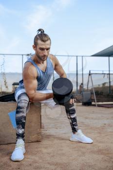 Strong man doing exercise with dumbbell, street workout. Fitness training on sports ground outdoor, male person pumps muscles, active urban lifestyle