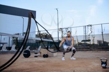 Athletic man doing exercise with ropes, street workout, crossfit. Fitness training on sports ground outdoor, male person pumps muscles, active urban lifestyle