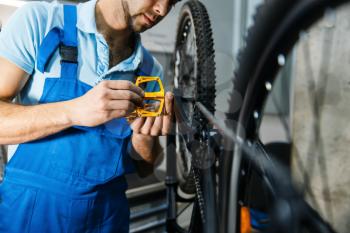 Bicycle repair in workshop, man installs pedals. Mechanic in uniform fix problems with cycle, professional bike repairing service