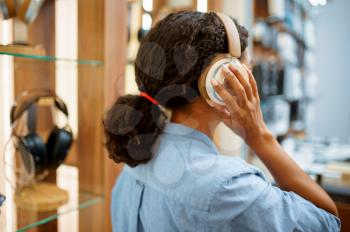 Woman trying on headphones in acoustics store, back view. Female person in audio shop, showcase with earphones on background, buyer in multimedia salon