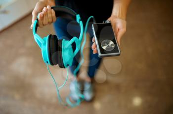 Girl showing headphones and phone in audio store, music fan. Female person in music shop, showcase with earphones on background, buyer in multimedia salon
