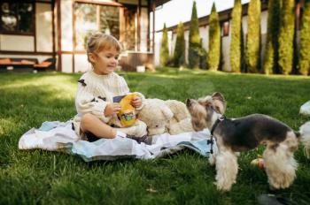 Kid play with teddy bear in the garden. Child with soft toy sitting on the lawn on backyard. Little girl having fun on playground outdoors, happy childhood