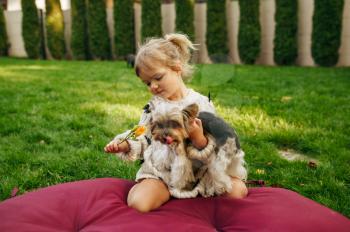 Kid embracing funny dog in the garden, best friends. Child with puppy sitting on the lawn on backyard. Little girl and her pet having fun on playground outdoors, happy childhood