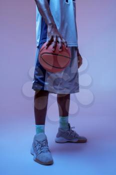 Strong basketball player hand holds ball in studio, neon background. Professional male baller in sportswear playing sport game, tall sportsman