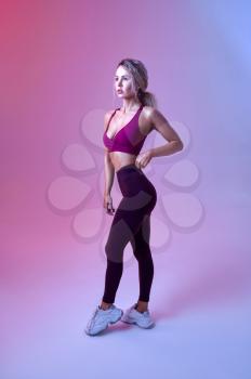 Young sexy woman with slim body poses in studio, neon background. Sportswoman at the photo shoot, sport concept, active lifestyle motivation