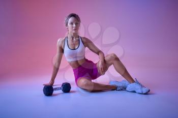 Sexy sportswoman poses with dumbbell in studio, neon background. Fitness woman at the photo shoot, sport concept, active lifestyle motivation