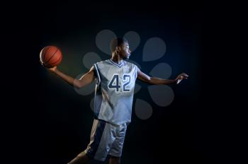 Basketball player with ball, practicing in action in studio, black background. Professional male baller in sportswear playing sport game.