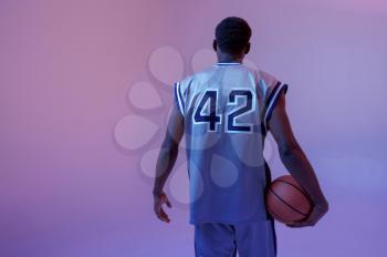 Basketball player poses with ball in studio, back view. Professional male baller in sportswear playing sport game, tall sportsman