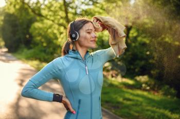 Morning training in park, woman in headphones listens to music on walkway. Female runner goes in for sports at sunny day, healthy lifestyle, jogger on outdoors workout