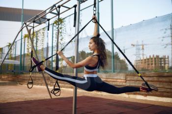 Woman with perfect body doing stretching exercise with ropes on sports ground outdoors. Slim female person in sportswear, outside fitness training, fit workout