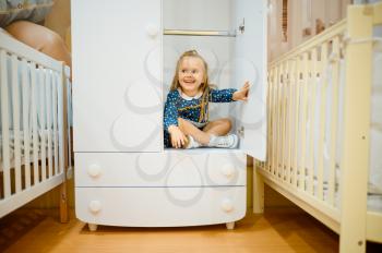 Smiling little girl sitting in wardrobe near baby bed in kid's store. Adorable child at the showcase in children's shop, happy childhood, gaughter makes a purchase in shop