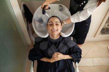 Hairdresser washes woman's hair, top view, hairdressing salon. Stylist and client in hairsalon. Beauty business, professional service