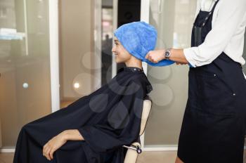 Hairdresser puts towel on woman's hair, side view, hairdressing salon. Stylist and client in hairsalon. Beauty business, professional service