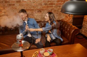 Love couple smokes at the table in hookah bar. Shisha smoking, traditional bong culture, tobacco aroma for relaxation, resting with hooka