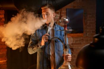 Young man blows smoke in hookah bar, hooka. Shisha smoking, traditional bong culture, tobacco aroma for relaxation, rest with hooka