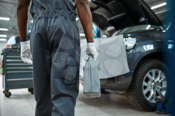 Male mechanic holds oil canister, car service. Vehicle repairing garage, man in uniform, automobile station interior on background